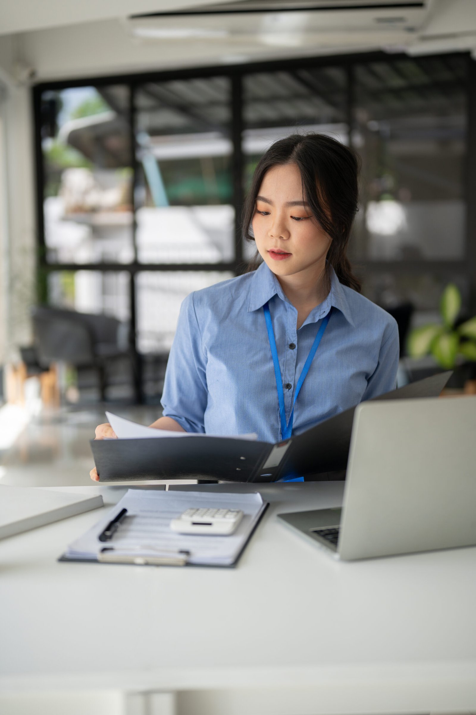 A portrait of a professional Asian businesswoman or female manager examining business documents at her desk in a modern office.